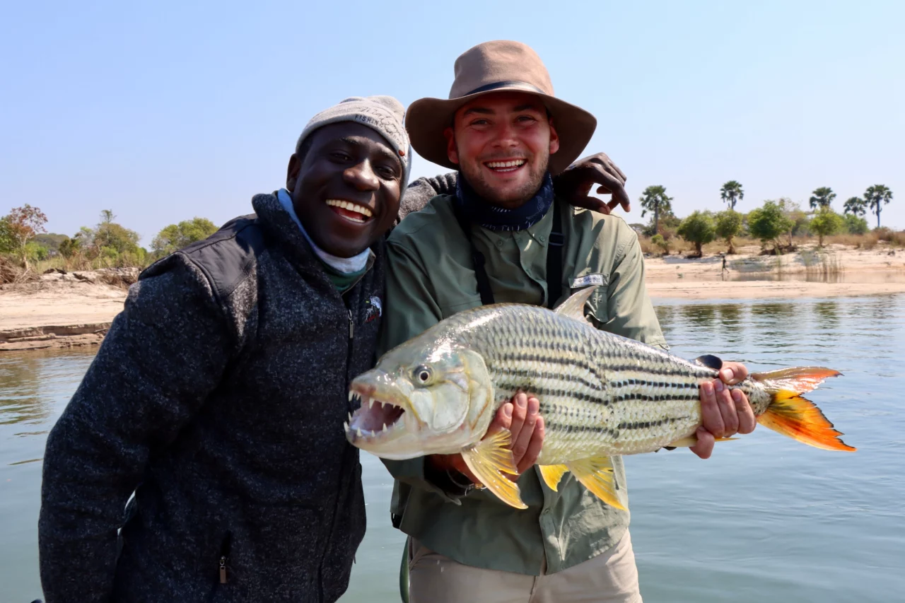 Friendly faces captured near a river located in Western Zambia. These two guys are smiling for the camera while holding a massive Tigerfish.  This was captured while traveling the Land of Lozi with Voetsporerentals