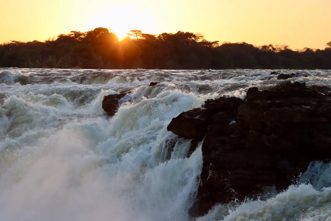 Scenic waterfall in a river captured while traveling with Voetsporerentals in the Land of Lozi. Beautiful sunset in the backround as the water is splashing in the river. 